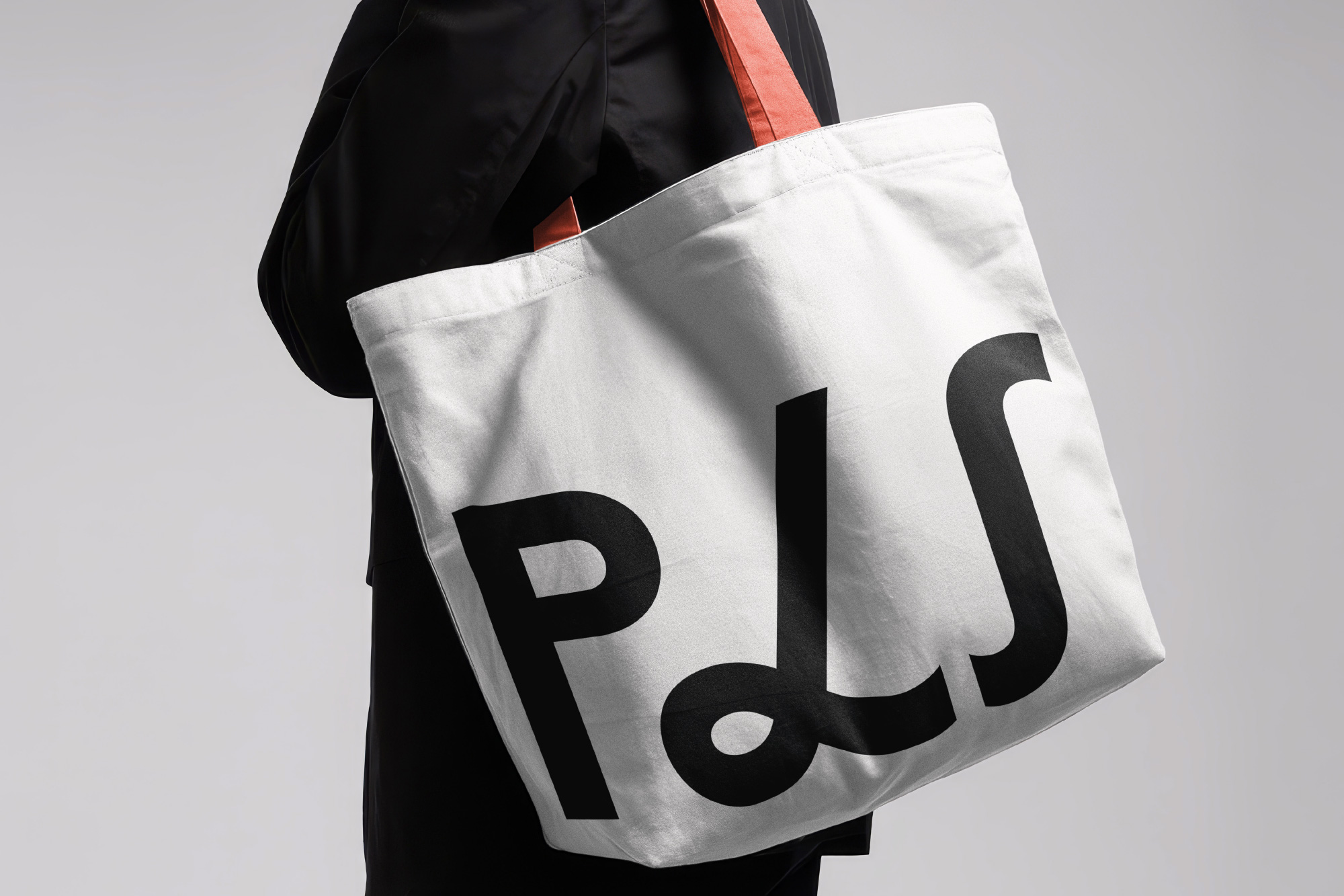 Person in black holds a white tote bag with large black "PLS" text and red handles.